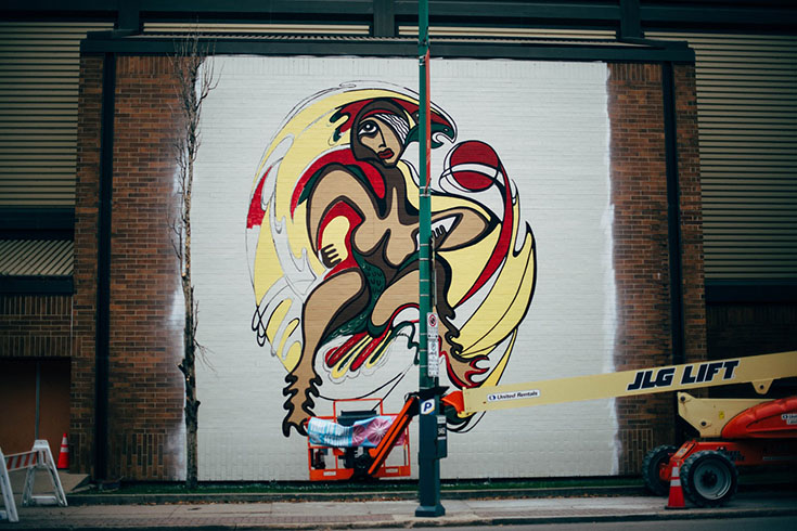 Photo of "Thunderbird Woman" mural on the north-facing exterior wall of Duckworth Centre. The mural is a reproduction of a Daphne Odjig work and depicts a woman-bird hybrid.