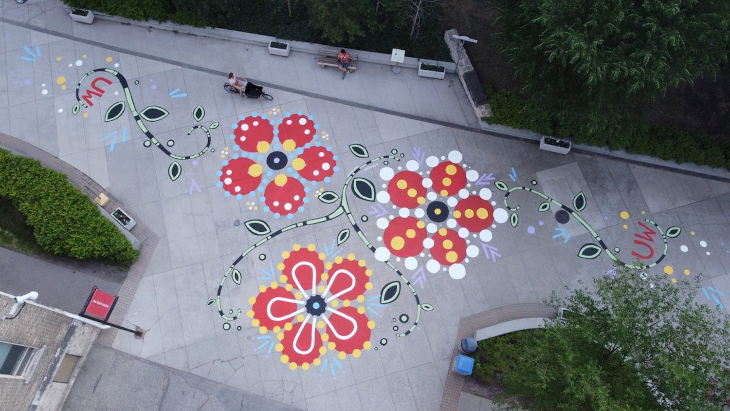 Image of sidewalk mural along Marsha Hanen Way at the University of Winnipeg. The mural shows three red flowers in the Métis floral beadwork style, composed of various sized dots.