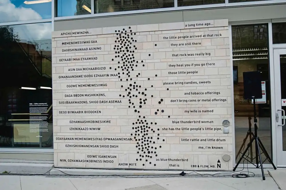 Image of ASIN public artwork on the Axworthy Health and RecPlex at the University of Winnipeg by Ebb and Flow First Nation and Eduardo Aquino. The mural is composed of etchings of a poem in both English and Ojibwe.