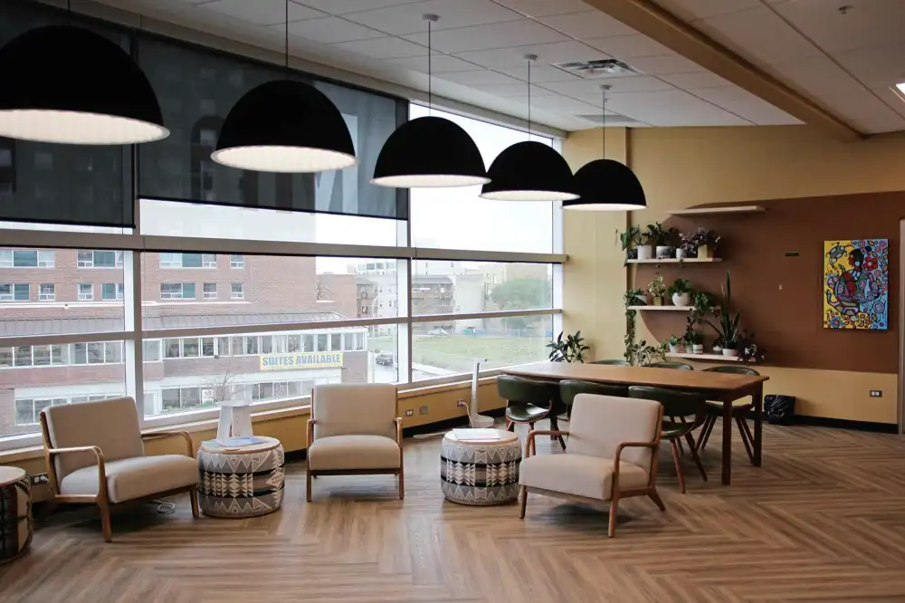 Image of Aabijijiwan New Media Lab interior. The image shows three custom designed chairs by Destiny Seymour made of wood and off white textiles. Between the chairs are drum stools upholstered in fabric with geometric designs inspired by Anishinaabe patterns.