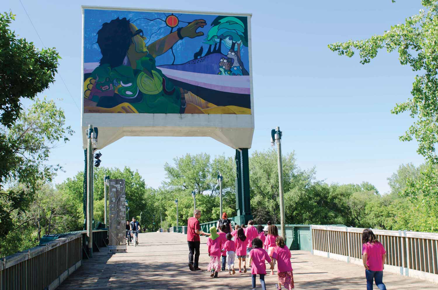 The rehabilitated Rail Bridge in summer 2015. On the counterweight is a colourful mural by Aboriginal artist Mike Valcourt. A group of young girls wearing pink shirts are being led across by a few adults.