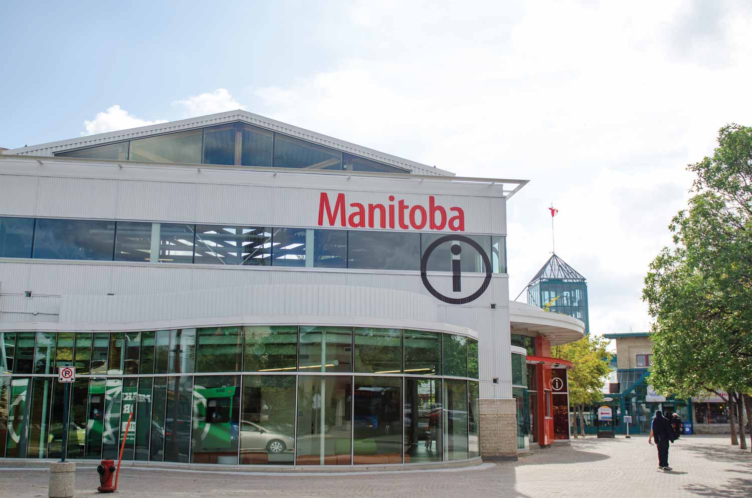 Travel Manitoba's glass windows are reflecting vehicles from the street. The Forks Market tower can be seen in the background.