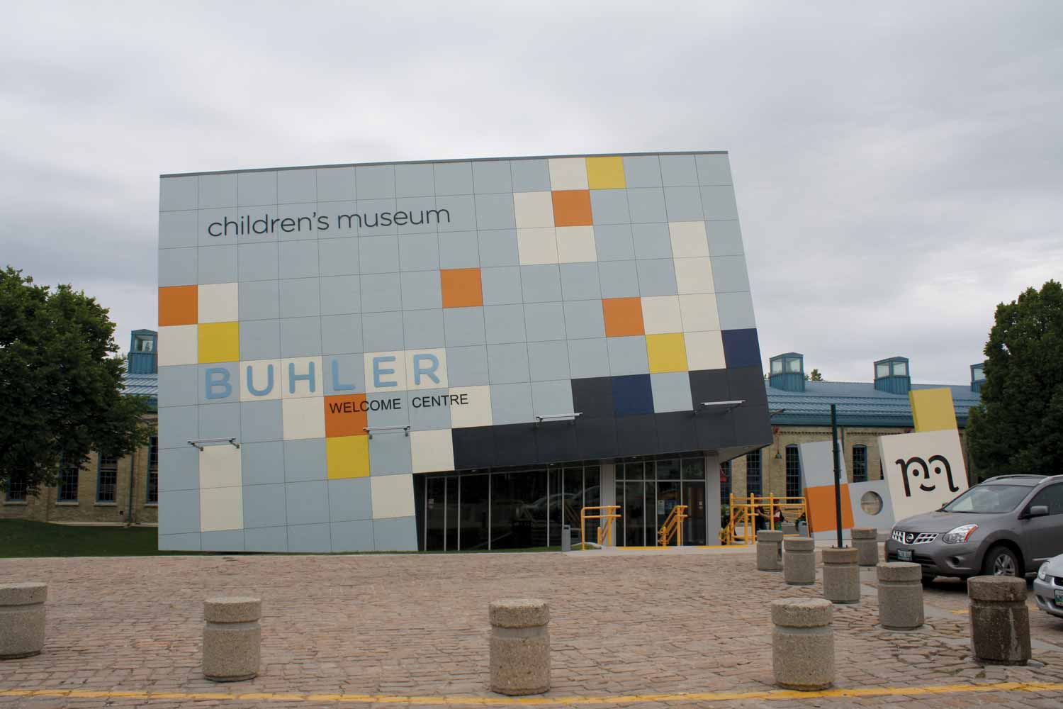 The Welcome Centre addition to the Children's Museum. More modern in style, it is blue, slightly askew, and has a grid of white, yellow, and orange squares as decoration.