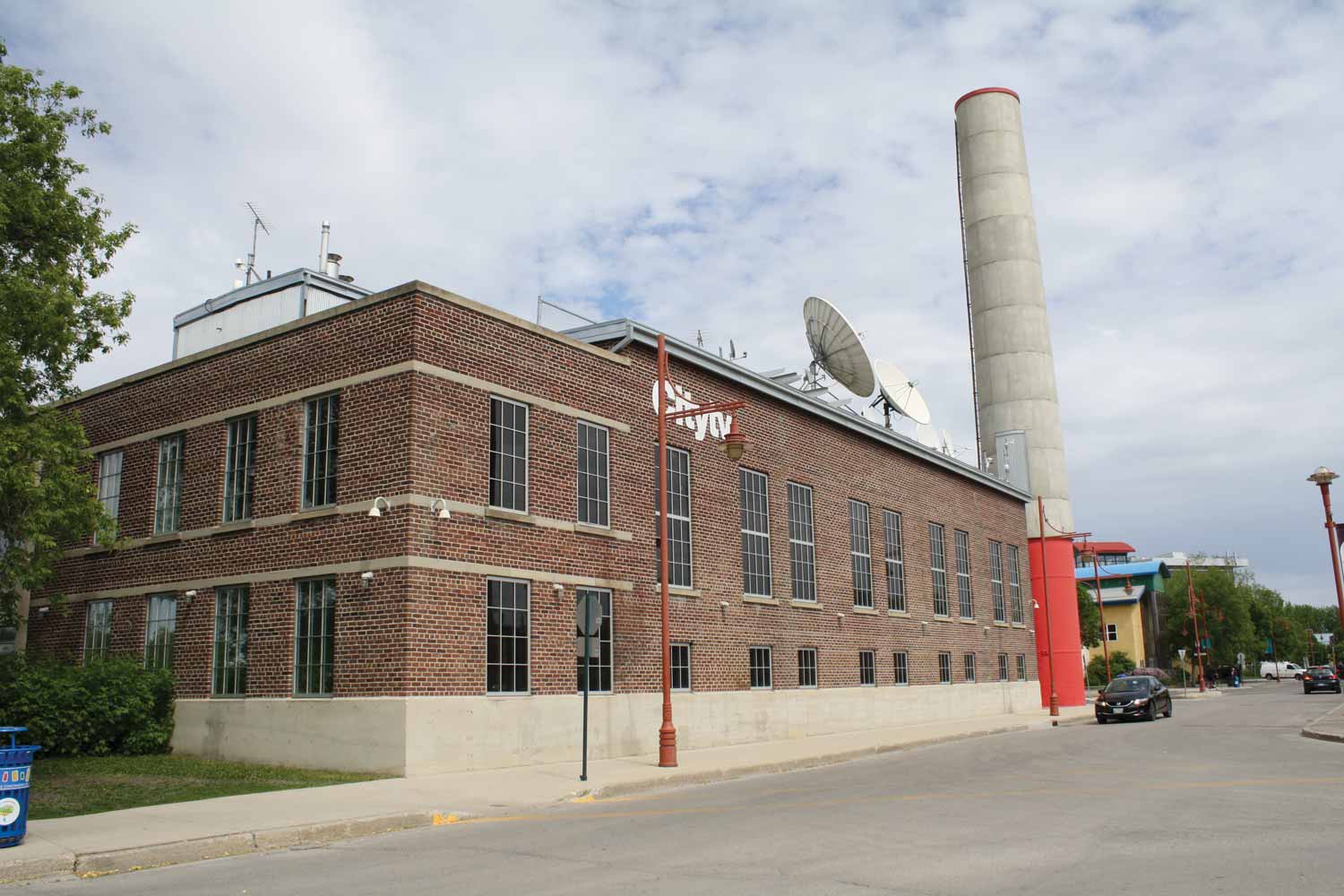 The CityTV building on a summer day. It is built of brown brick, with a red and grey smoke stack behind it.