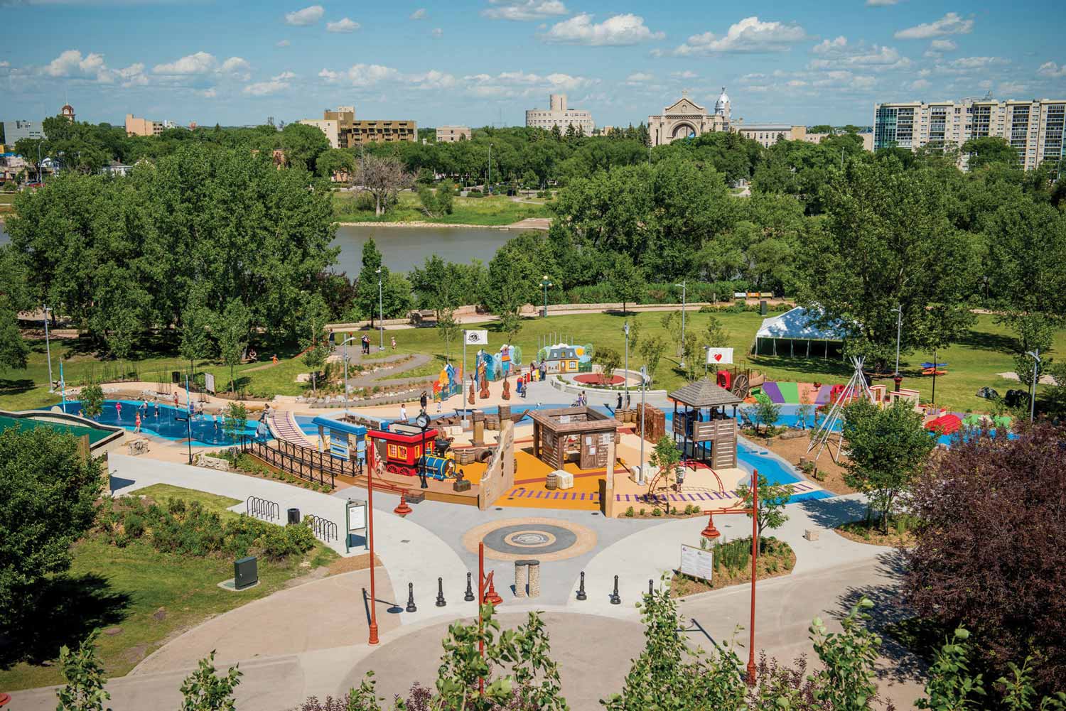 Aerial photo of a colourful park with a train, small buildings, splash pads, teepee, and play structures