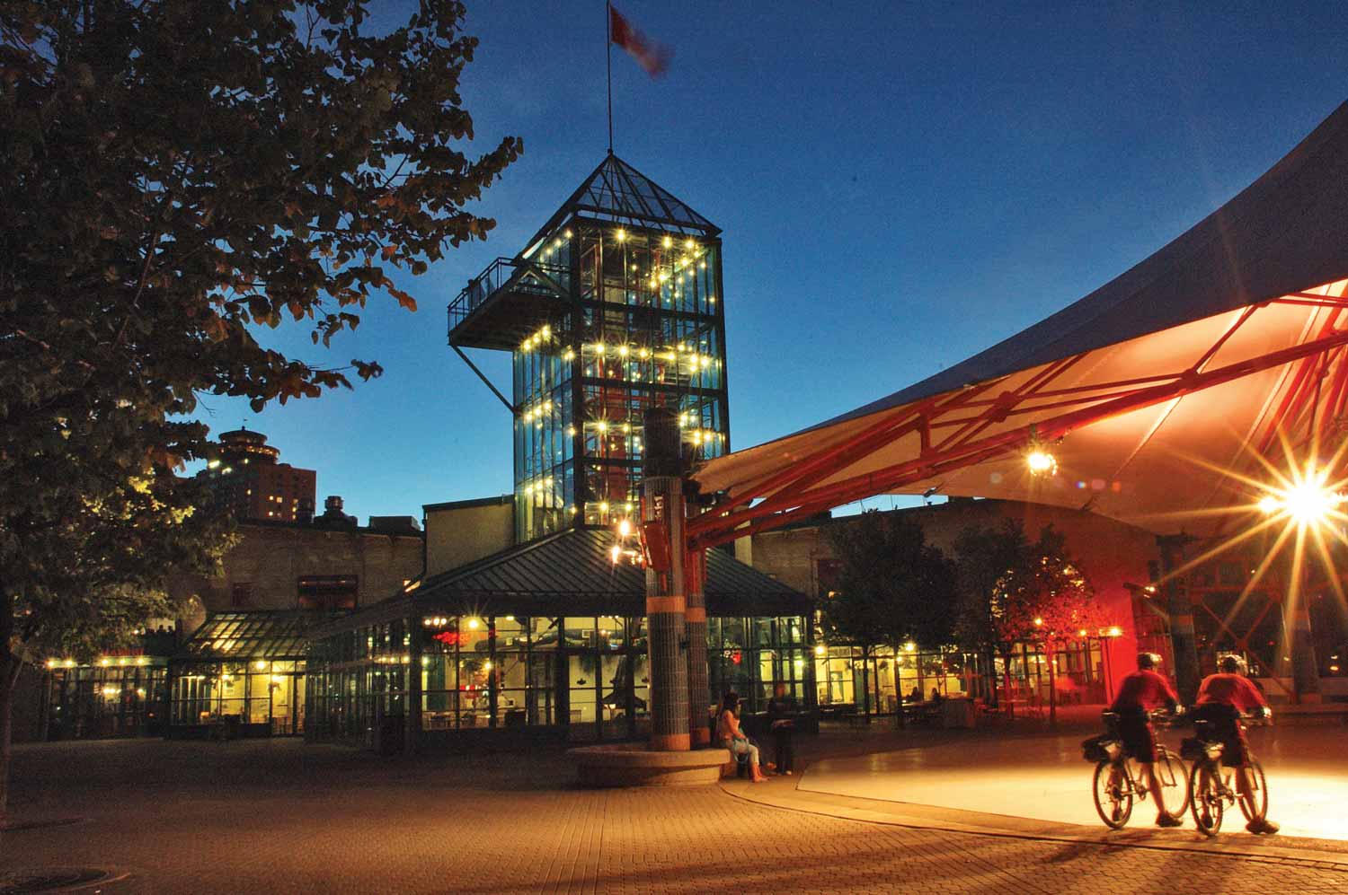 The Forks Market on a summer night, with its floor-to-ceiling glass windows lit up by interior lighting.