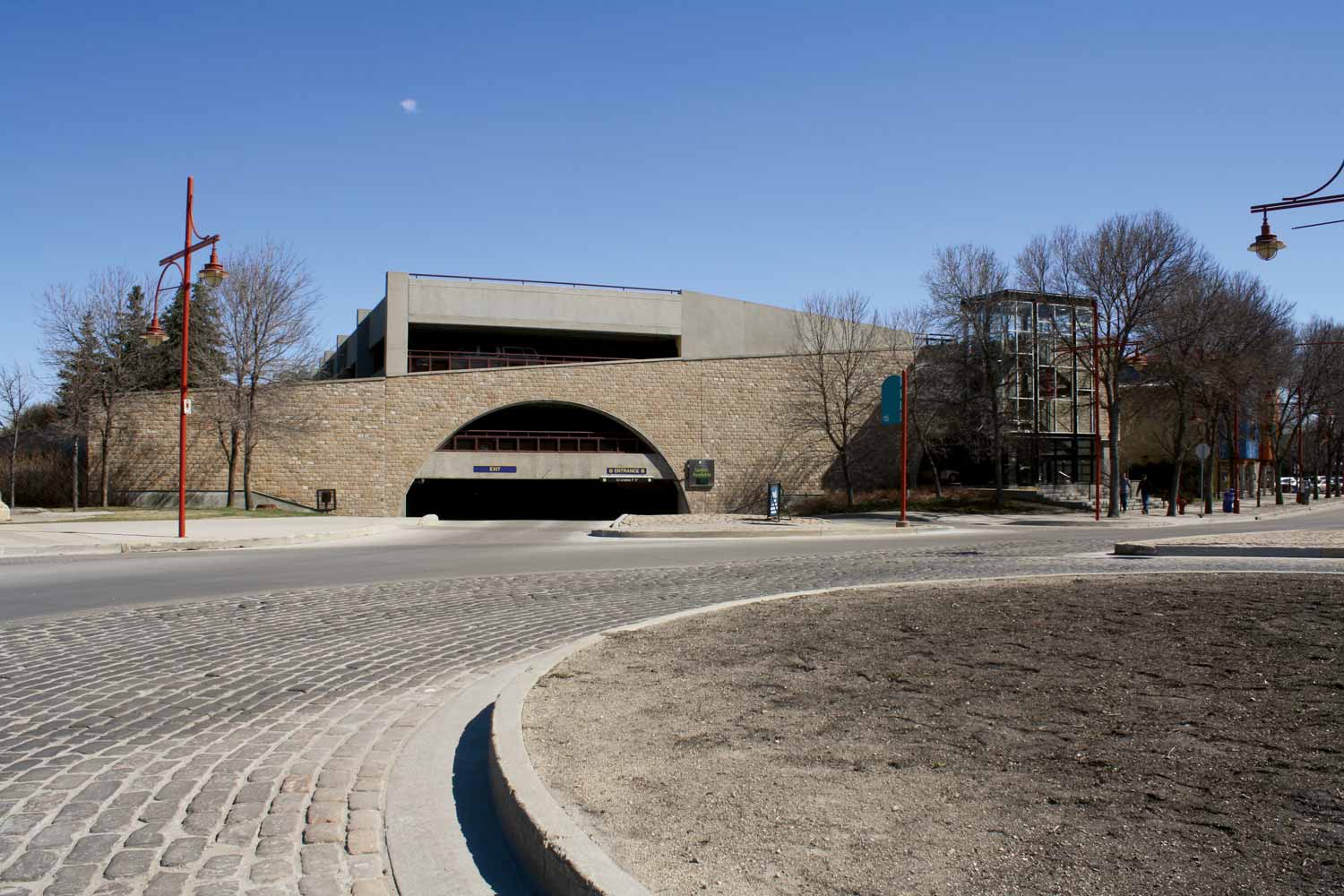 The entrance of The Forks Parkade is a semicircle. Beyond the entrance section, the slightly taller parkade is sitting next to a glass-enclosed staircase to the different floors.