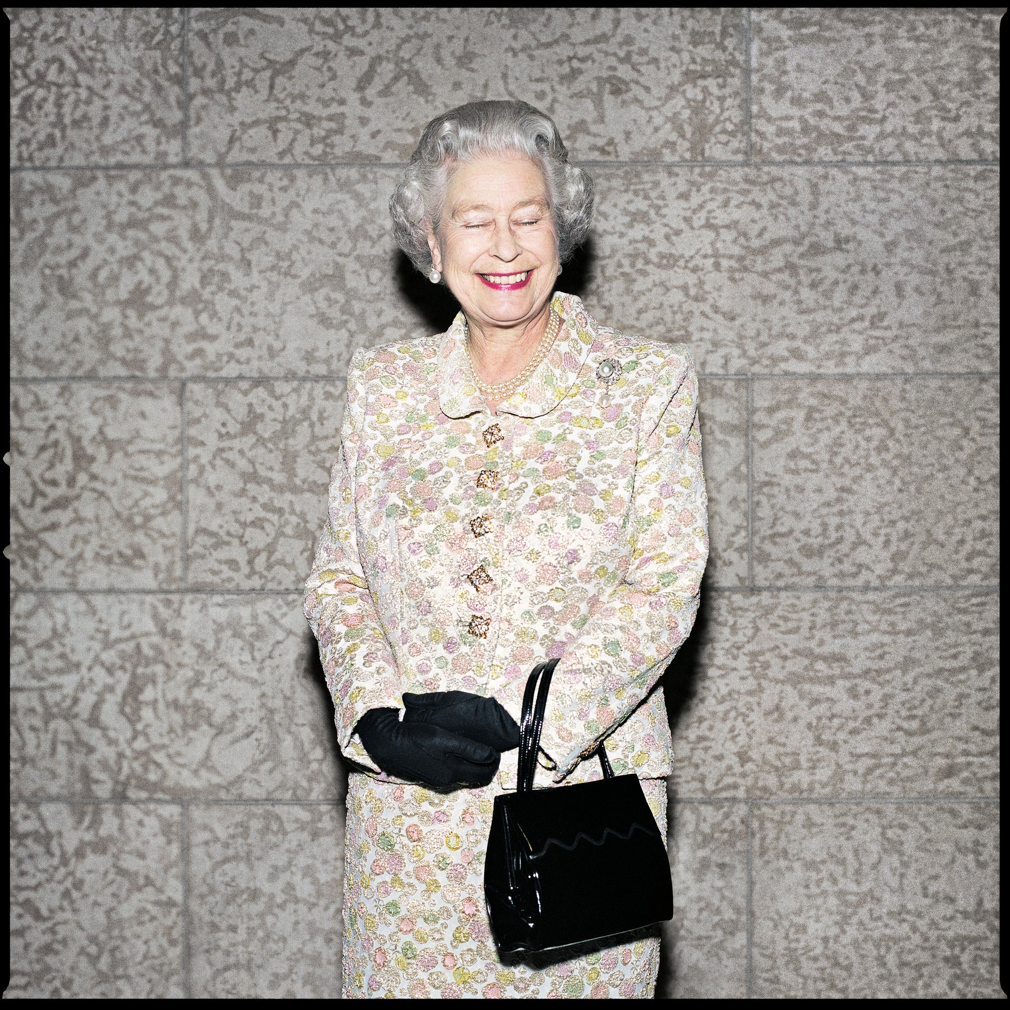 Queen Elizabeth II standing in front of a Tyndall stone wall.