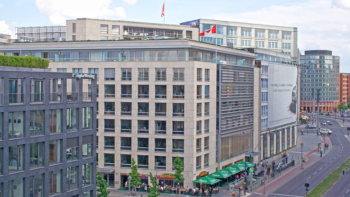 Image shows the exterior of a multi-storied building on a busy street. There are large rows of windows on every floor.