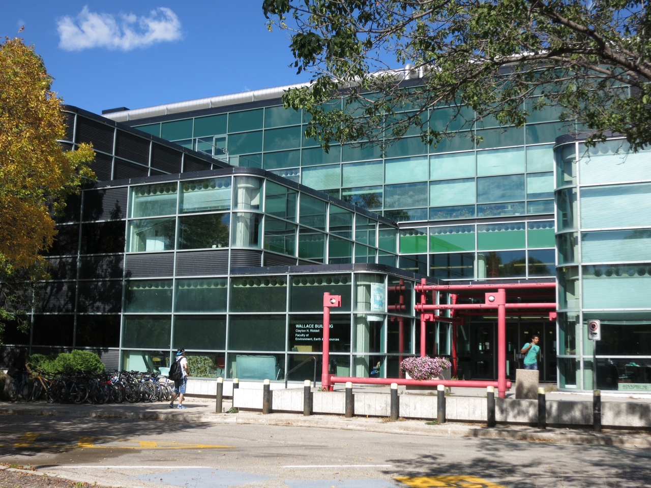 Image shows large building clad entirely in glass. There are bright red pipes at the entrance.
