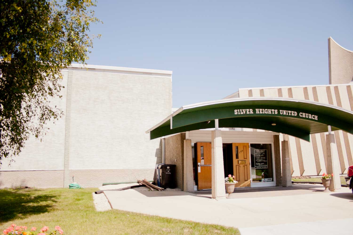 Image shows the exterior of Silver Heights United Church. A dark curved canopy extends generously over entrance.