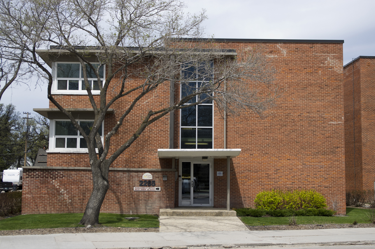 Image shows the exterior of the apartments. The glass window panels ascends from the main entrance.