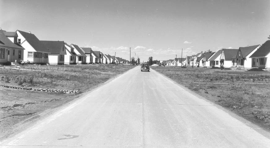 Image shows a street of homes, with a car down the road.