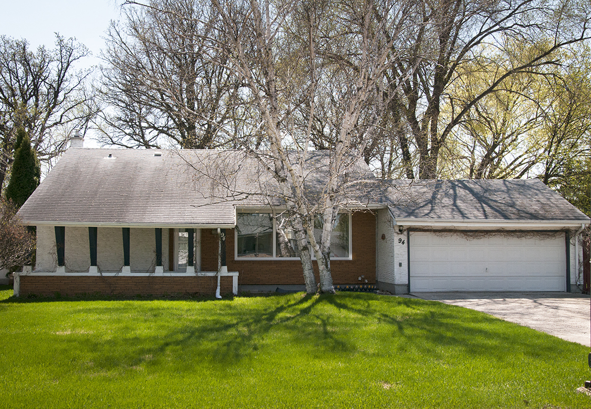 Image shows a one-storey home with a dark brick exterior and columns on the porch.