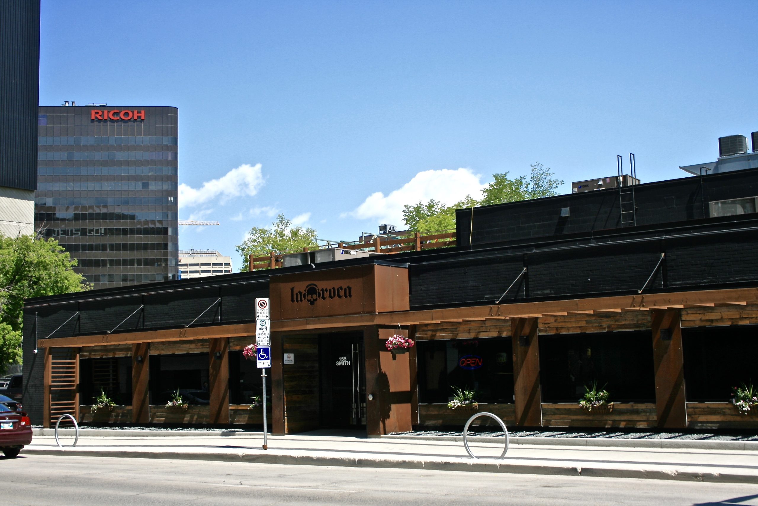 The exterior of the renovated 155 Smith Street. The building is black with wood accents. There is a sign for La Roca with a skull.