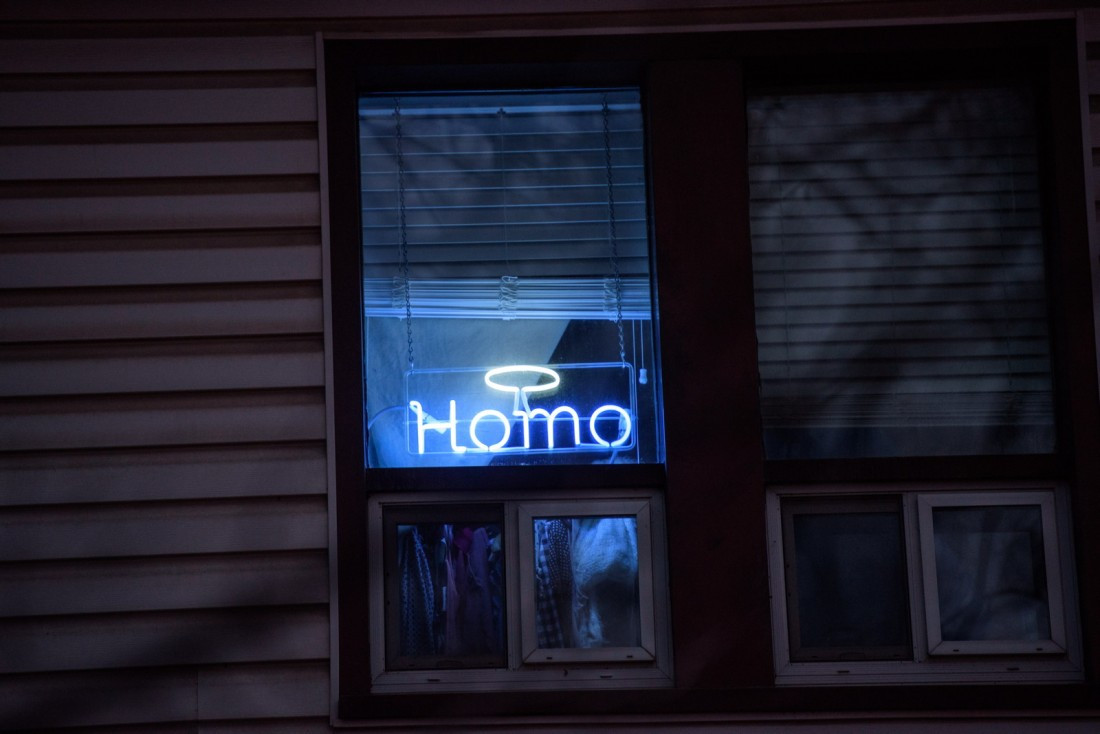 A neon sign that says "Homo" with a halo above it in the window of the house.