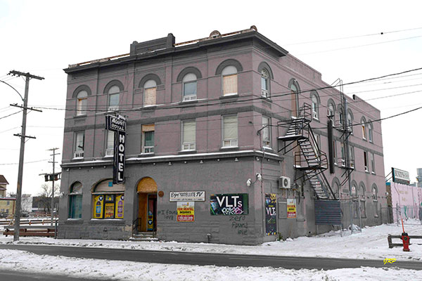 The exterior of The Mount Royal Hotel in the winter. The building is grey and there is a sign that says "MOUNT ROYAL HOTEL" above the door. There is a fire escape on the right-hand side of the building.